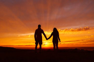 Gün batımında aşık olan tanınmayan bir çift. Mutlu adam ve kadın el ele tutuşuyor.