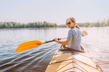 Genç mutlu kadın nehirde seyahat ediyor. Arkadan bak. Yüzü kameraya dönük. Gezgin gülümsüyor.