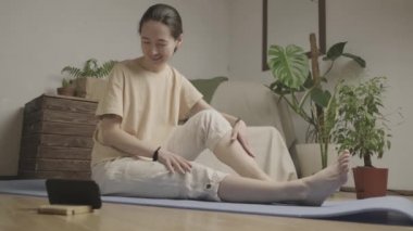 Genç kadın bacaklarını ve vücudunu esnetiyor. Ders internet üzerinden akıllı telefon kullanılarak veriliyor. Kilitleme sırasında evde.. 