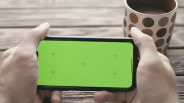 Kahve molası sırasında yeşil ekranlı akıllı telefon kullanan bir adam. Cep telefonu ekranında model krom anahtarı.