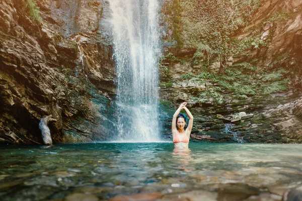 Schöne Frau im Badeanzug vor dem Hintergrund eines Wasserfalls in der Lagune. — Stockfoto