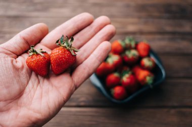 Adamın elinde iki tane çilek var.