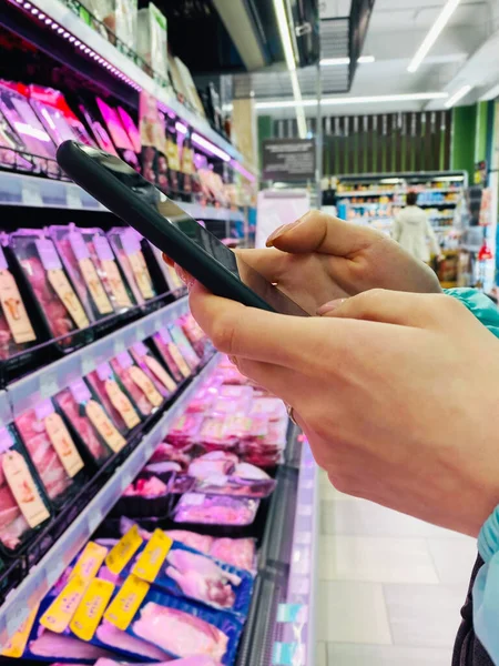 Nierozpoznawalna kobieta kupująca w supermarkecie z komórką w rękach — Zdjęcie stockowe