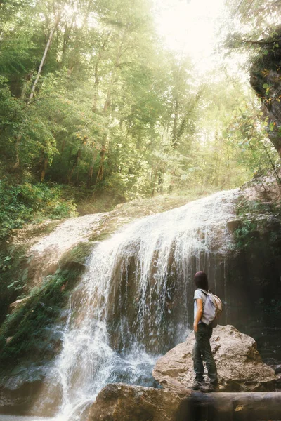 バックパック付きの女性観光客が滝の横を歩く. — ストック写真