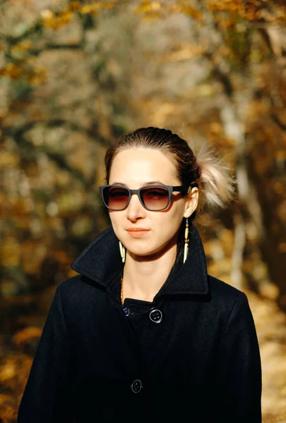 Retrato de uma mulher elegantemente vestida com um casaco preto e óculos de sol. — Fotografia de Stock