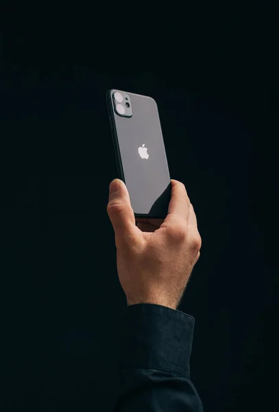 Το αρσενικό χέρι κατέχει ένα iPhone 11 σε μαύρο φόντο, το λογότυπο μήλο αναπτύσσεται στην κάμερα. — Φωτογραφία Αρχείου