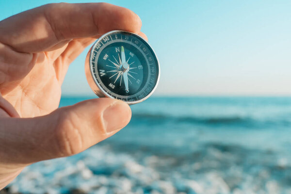 Man traveler holds a compass in his hand. In the background is a seascape.