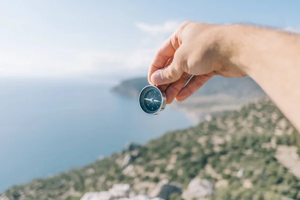 Kompas in mannelijke handen op de achtergrond zee en bergen. — Stockfoto