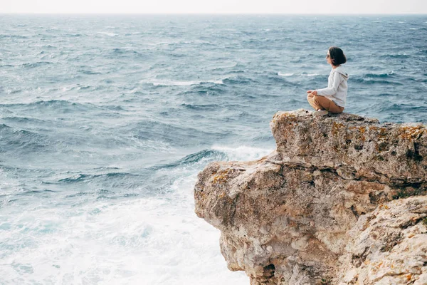 젊은 여자가 바위가 많은 해변 가장자리에 앉아 있다. — 스톡 사진