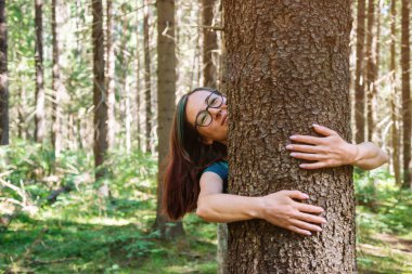 Genç neşeli kadın parkta ya da ormanda bir ağaca sarılıyor..