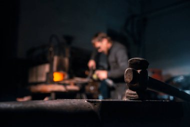 Önünde çekiç, arkasında demirci olan örs..