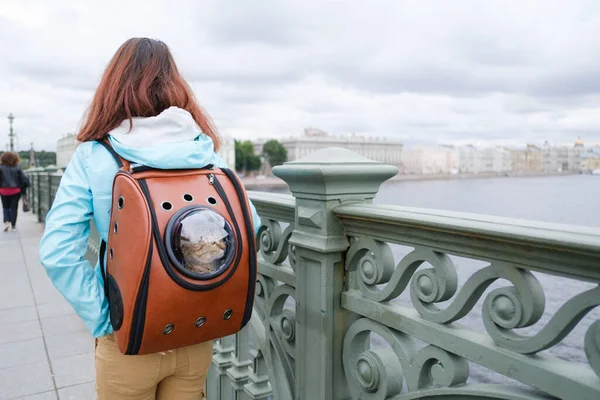 Femme transporte son chat dans la rue dans un sac à dos avec un hublot. — Photo