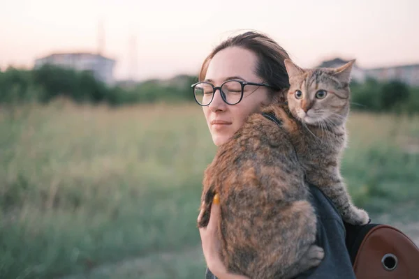 Dziewczyna spaceruje z ciekawskim kotem na ramieniu w parku miejskim latem. — Zdjęcie stockowe