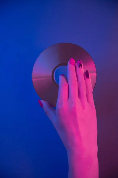 La mano femenina sostiene un disco compacto sobre un fondo azul en luz de neón púrpura. — Foto de Stock