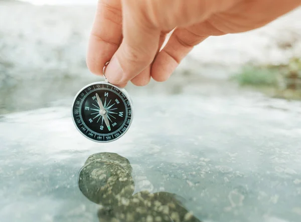 Människan håller en kompass ovanför vattnet. — Stockfoto
