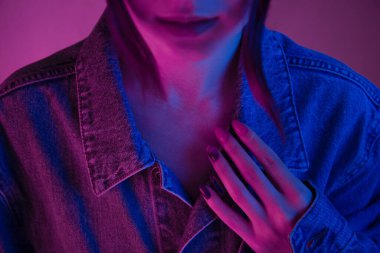 Portrait of unrecognizable young woman in pink neon light in denim jacket.
