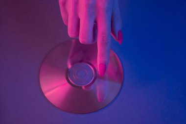 Womans hand touches a finger to a CD on a blue background.