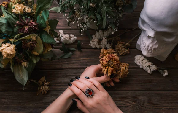 Weibliche Hände mit schwarzer Maniküre. Verwelkte Blumen und ein Totenkopf. Romantische Gotik. — Stockfoto