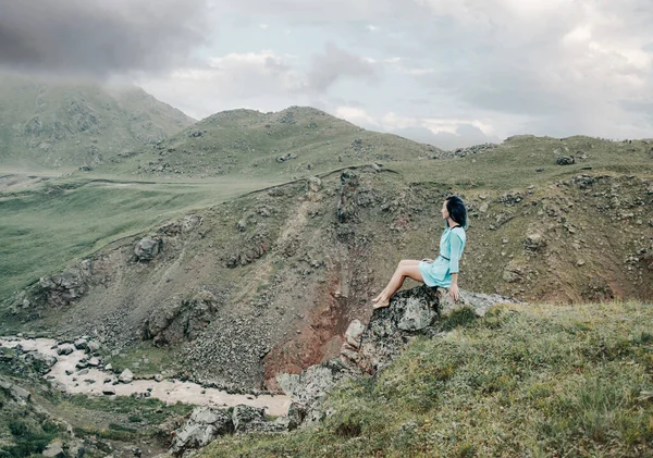 Traveler woman sits on a stone in the mountains. — Stock Photo, Image