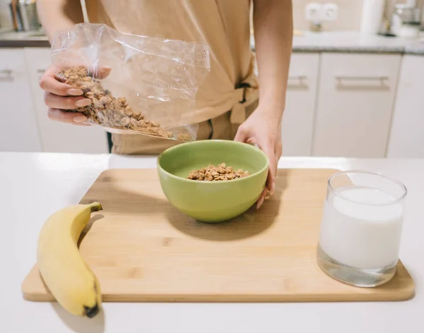 Joven mujer vierte granola en un plato para el desayuno. — Foto de Stock