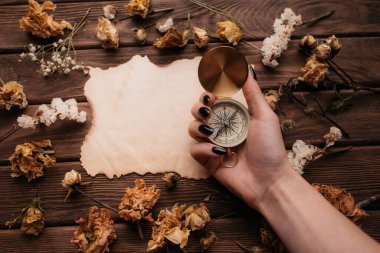 Kuru çiçeklerin arasındaki boş eski bir kağıdın önünde pusulayı tutan kadın..