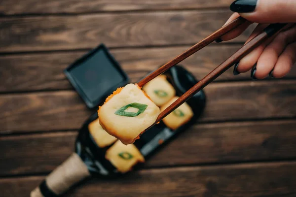 Mano femenina sosteniendo rollo de sushi con palos de madera. — Foto de Stock