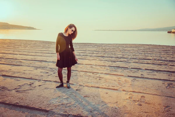 Modisches Mädchen steht bei Sonnenuntergang am Strand — Stockfoto