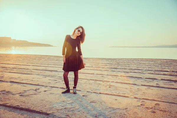 Modieus meisje permanent op strand bij zonsondergang — Stockfoto