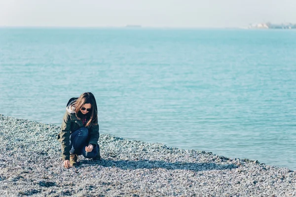 Jonge vrouw verzamelt stenen aan kust — Stockfoto