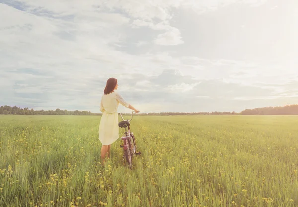 Girl walking with bicycle on meadow — Stock Photo, Image