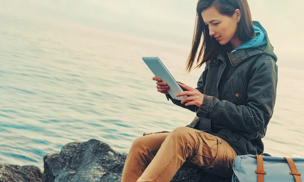 Traveler girl sitting on coast with tablet — Stock Photo, Image