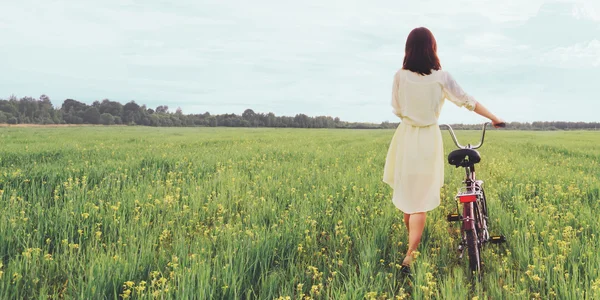 Girl walking with bicycle in meadow — Stock Photo, Image