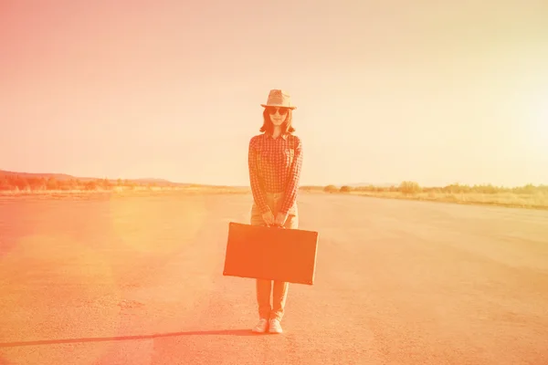 Женщина стоит на дороге с винтажным чемоданом — стоковое фото