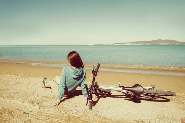 Meisje rusten op strand met het fiets — Stockfoto