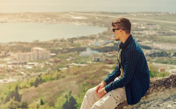 Hombre sentado en la cima de la montaña y mirando a la ciudad — Foto de Stock