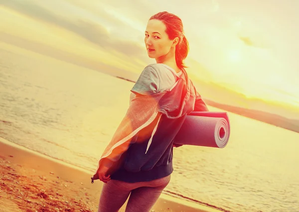 Vrouw met yoga mat permanent op strand — Stockfoto