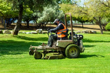 Man mowing or cutting the long green grass with a green lawn mower in the summer sun.
