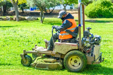 Man wearing black face mask mows the grass with lawn mower. Mow the lawns.