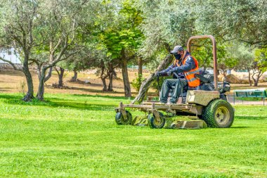 Man wearing black face mask mows the grass with lawn mower. Mow the lawns.