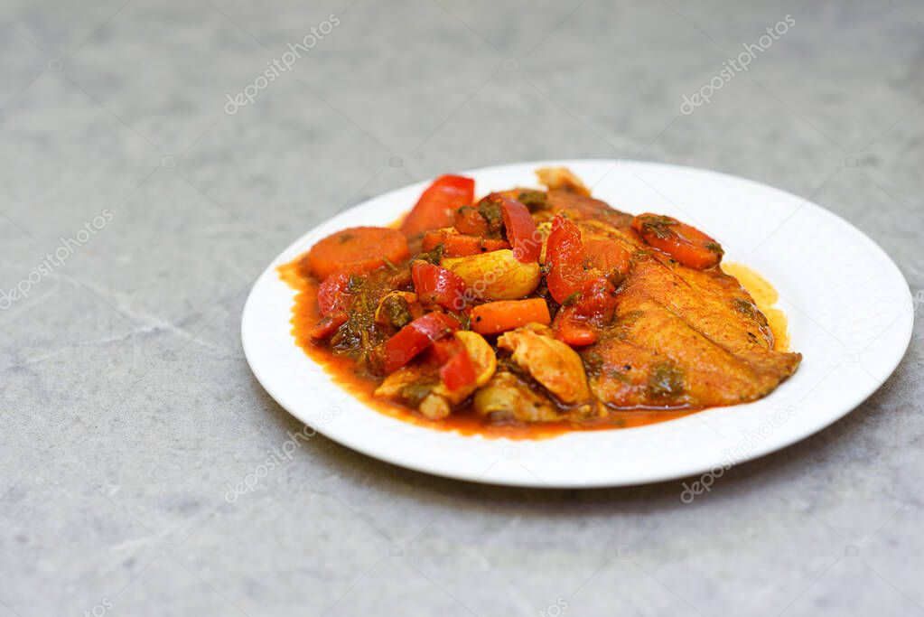 Fish in hot tomato sauce with vegetables on white plate. Home made tasty food ready to eat.