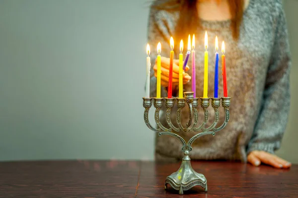 Jewish Woman Celebrating Holidays Hanukkah Alone DuringThe COVID-19 Pandemic. Woman Lighting Hanukkah Candles In A Menorah.