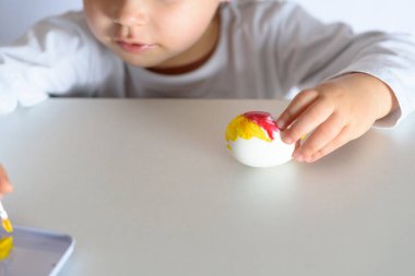Child hands painted Easter eggs, paints and brushes on white table. Preparation for the Easter. Kid hands draw with colors.