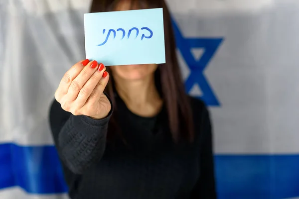 Mujer joven que lleva a cabo la votación frente a la cara en el fondo de la bandera israelí.Texto hebreo He votado en el papel de votación. —  Fotos de Stock