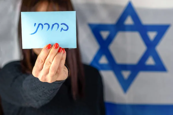 Fiatal nő tartja szavazólap eleje arc izraeli zászló háttér.Héber szöveg Szavaztam a szavazólapon. — Stock Fotó