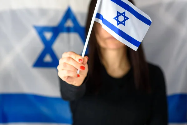 Jeune femme tenant le petit drapeau israélien devant le visage sur fond de drapeau israélien. — Photo