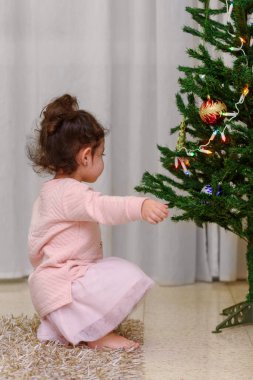 Halıda oturan at kuyruklu, Noel ağacının yanında oynayan sevimli çocuğun yan görüntüsü..