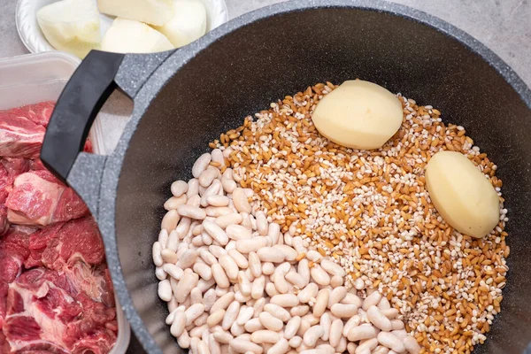 Raw Beef Being Added To A Saucepan Of Potatoes, Onion, Pearl Barley, Beans And Wheat Grains. — Stock Photo, Image