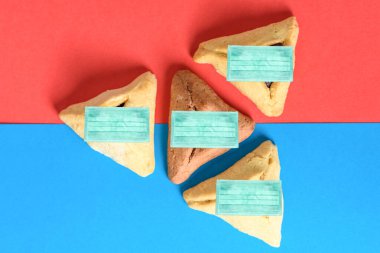 Yahudi bayramı için Hamantash üçgen kurabiyeleri. Kırmızı ve mavi arka planda yüz maskesi takıyorlar..