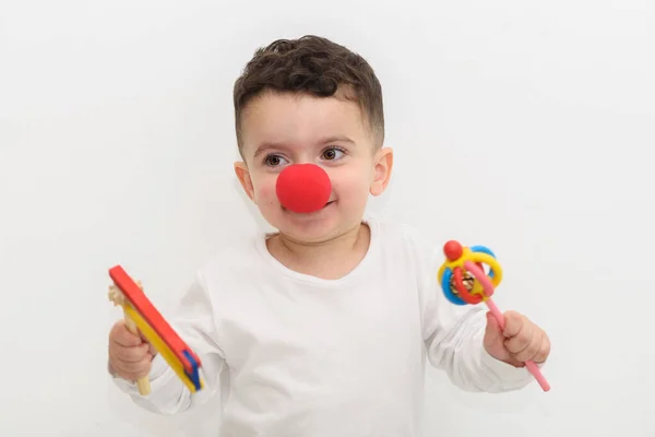 Portrait of laughing little boy with a clown nose and graggers on white background. — Stock Photo, Image