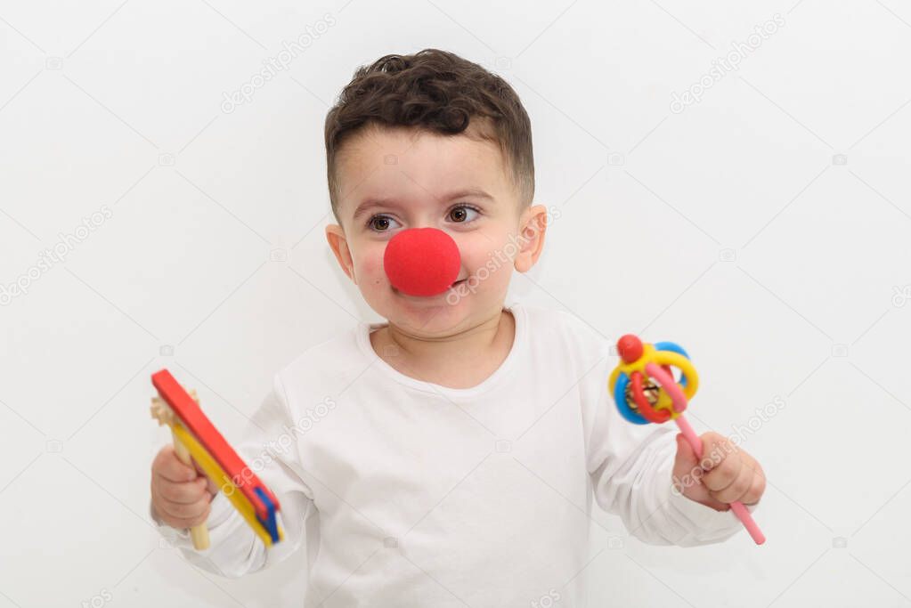 Portrait of laughing little boy with a clown nose and graggers on white background.